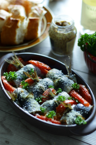 Baked sardines stuffed with tomatoes, presented on a rustic plate alongside a sake cup.