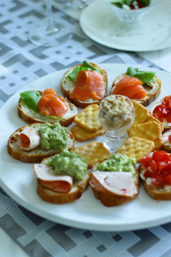 Assorted appetizers including smoked salmon on baguette slices and avocado dip, served with sake.