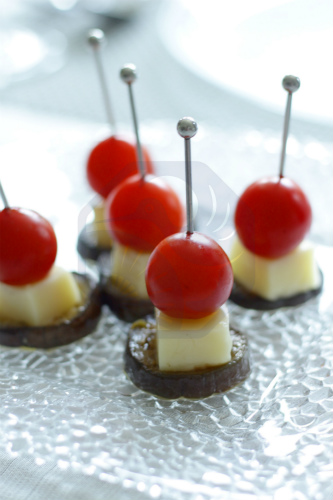 Skewered appetizers of cherry tomatoes, cheese, and eggplant, accompanied by a glass of cold sake